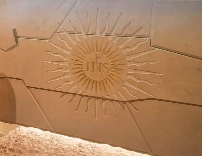 Stone tomb carved with the IHS monogram in a gilded sunburst