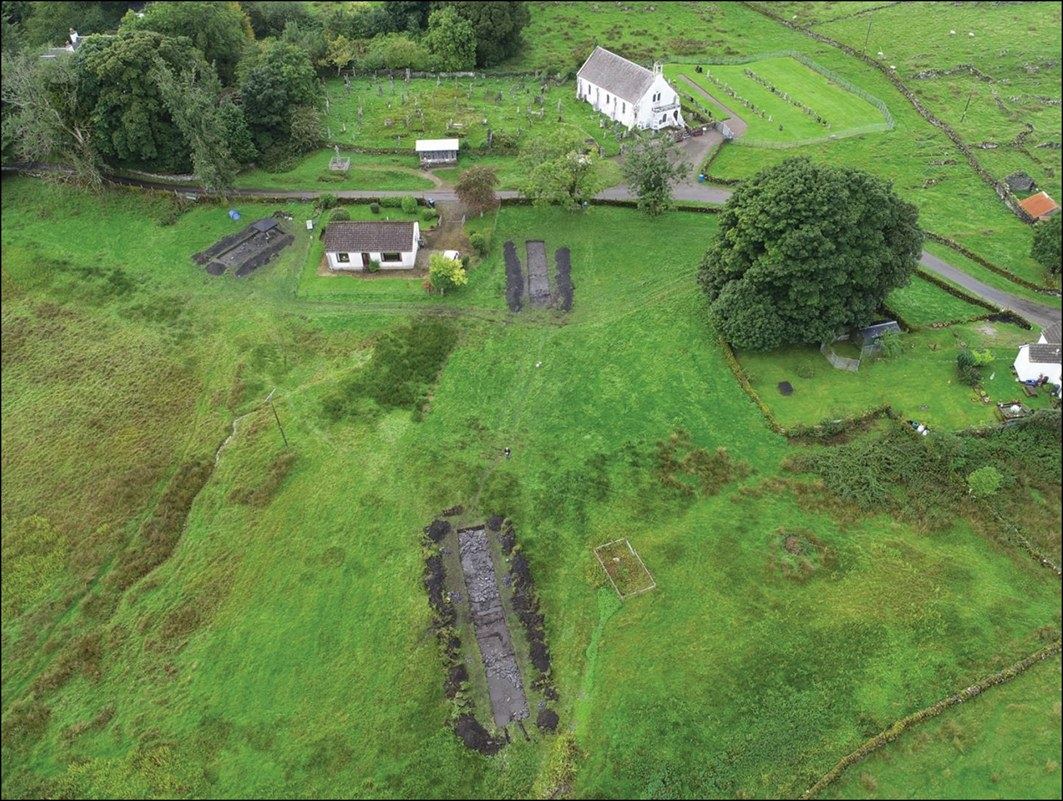 Aerial view of excavation trenches in a green field beside Lismore’s white parish church
